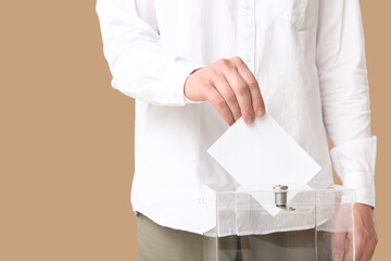 Voting young man near ballot box on beige background, closeup