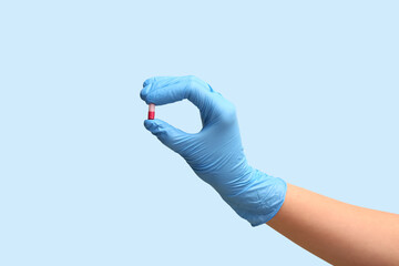 Hand of doctor in glove with pill on blue background