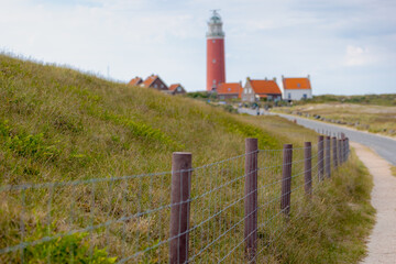 Typical landscape of Island in north sea with blue sky, Sand dunes with and european marram beach grass, Blurred Eierland Lighthouse red tower, De Cocksdorp, North Holland province, Texel, Netherlands
