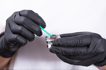 Close-up of a gloved hand holding a makeup brush and an open container of brown powder makeup.