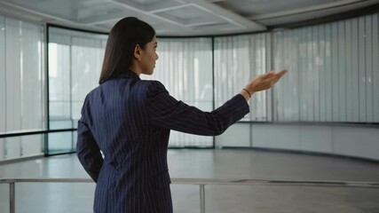 A woman in a suit is pointing at something. She is wearing a blue suit and has a hand on her hip