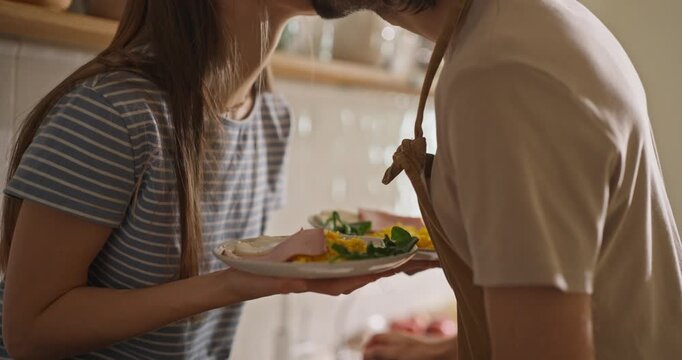 Close up of guy making breakfast presentation while girl holding plates in cozy kitchen while loving couple cooking breakfast together