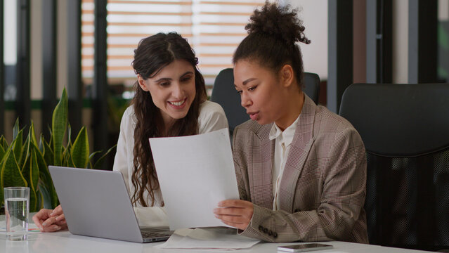 Multiethnic women business partners coworkers colleagues girls office managers African Caucasian businesswomen female team analyze documents together business consultation discuss sales graphs notes