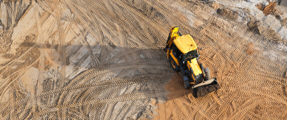 Yellow excavator working on sandy construction site with visible tire tracks from heavy machinery  
