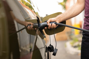 Closeup of man connecting plug to EV car for recharging, concept of zero carbon footprint tech....