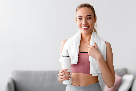 Glad european pretty young blonde fitness female blogger with bottle of water resting after workout at home. Health and body care athlete after training, sports indoor during covid-19 pandemic