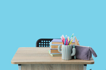 Modern school desk with books and stationery on blue background