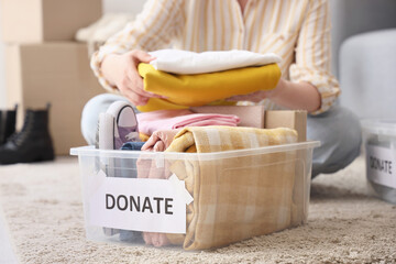 Young woman packing clothes into container for donation at home, closeup
