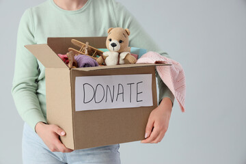 Young woman with box of toys for donation on light background