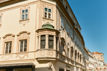 Photo of a historic house in Wachau, Austria with green bay window, decorative facade, and a street lined with houses extending into the distance under a blue sky.