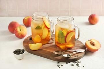 Wooden tray and glasses of tasty peach iced tea on white table near pink tile wall, closeup