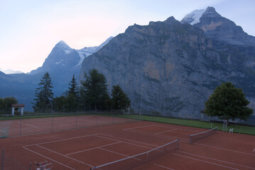 An elevated view of an empty clay tennis court with snow-capped mountains in the background during...