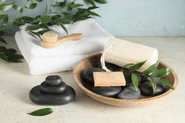 Composition with spa stones, green twig, bowl and loofah sponge on white table near blue wall,...