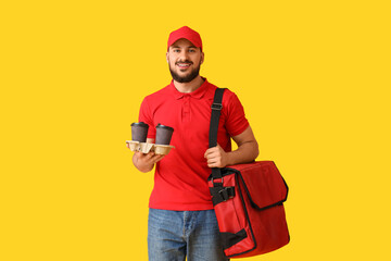 Male worker of food delivery service with bag and coffee cups on yellow background
