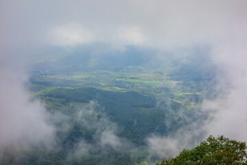 A breathtaking and moody vista of a vast, green valley and rolling hills is framed by thick, dramatic clouds from an elevated viewpoint on Skyline Drive in Shenandoah National Park.