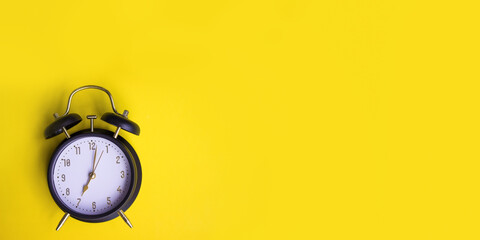 Black alarm clock showing seven oclock on yellow background with copy space.