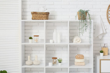 Shelf unit with bath accessories and plants near white brick wall