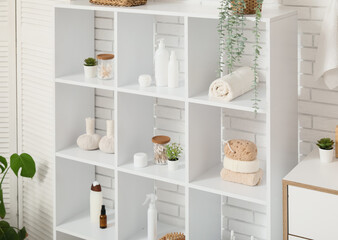 Shelf unit with bath accessories and plants near white brick wall