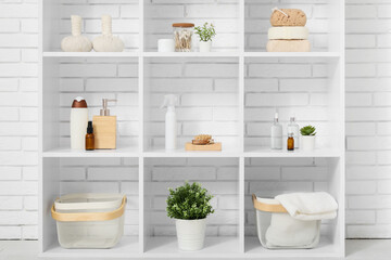 Shelf unit with bath accessories and plants near white brick wall