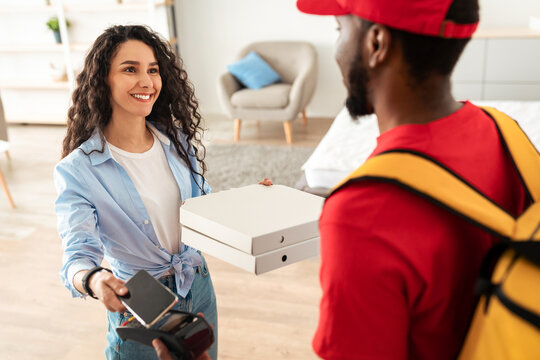Portrait of smiling woman making payment through wireless modern bank terminal. Customer paying using smartphone and NFC technology to courier for package delivery. Modern Futuristic Technology