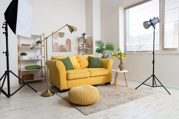 Photo shoot of living room with yellow sofa, shelf units and lighting equipment in studio
