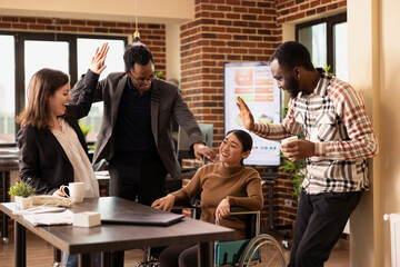Businesswoman with a disability sharing a joyful conversation with her multiethnic colleagues in modern workspace. Excited diverse employees celebrating a company achievement together in the office.