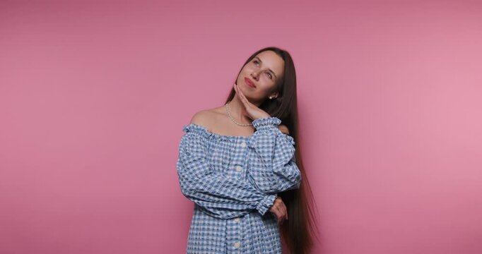 Woman in blue gingham dress poses thoughtfully against a pink background in a studio setting