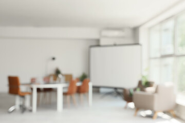 Blurred view of conference hall with desk, armchairs and projector screen