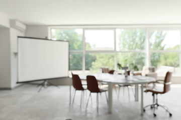 Blurred view of conference hall with desk, armchairs and projector screen