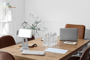 Blank tablet computer with water bottles on table prepared for business meeting in conference hall