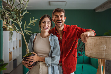 Happy couple decorating new home holding plant and lamp smiling