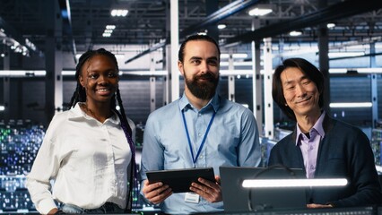 Portrait of smiling engineers in server room using AI to review infrastructure diagnostics. Cheerful IT coworkers in data center analyzing performance data using artificial intelligence, camera A