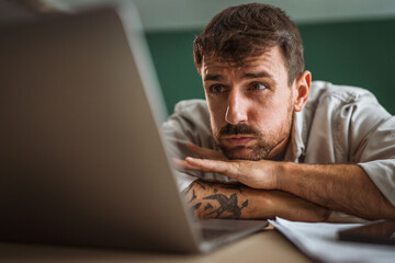 Tired freelancer looking at laptop at home office desk