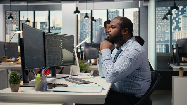 Day trader analyzes stock market price charts, doing thinking, making buy and sell decisions in prop firm office. Man doing brainstorming, placing client orders using trading platform
