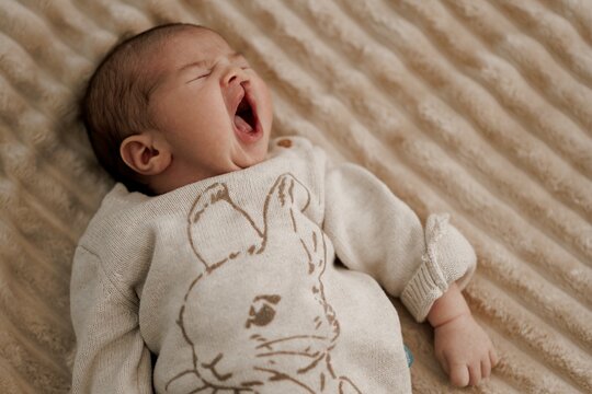 Yawning Baby in Rabbit Sweater on Beige Blanket