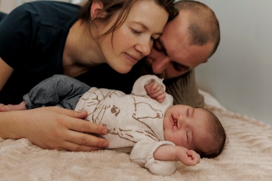 A couple lovingly embraces near a newborn baby in a hospital room.