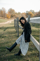 a portrait of a brunette girl dressed in a light dress and a knitted sweater walking in the...