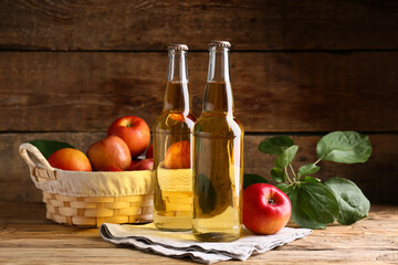 Bottles of fresh apple cider and wicker basket with fruits on wooden background