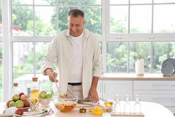 Mature man making apple cider at table in kitchen