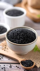 Black sesame seeds fill a shallow bowl, alongside a wooden spoon and a background of natural textures.