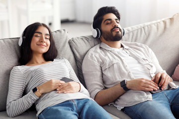 Free time for relax, rest at home, audio app at home. Calm satisfied happy young arab couple with...
