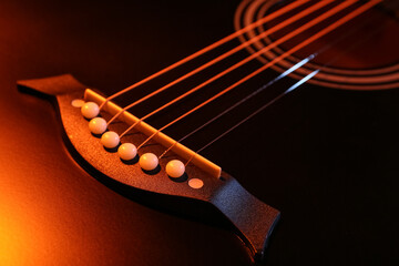 Fototapeta premium Modern black guitar with orange light as background, closeup
