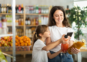 Mother and daughter choose bottles of juice and scan QR code with smartphone