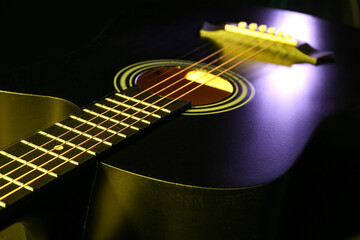 Acoustic guitar with yellow light on strings on black background, closeup
