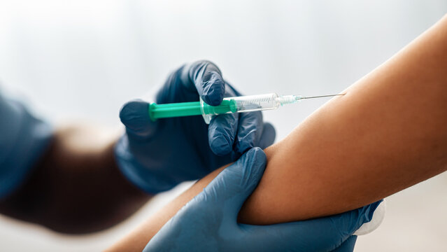 Covid-19 or coronavirus vaccine and immunization, prevention pandemic. Young african american doctor in protective gloves and uniform make injection to patient in clinic, close up, free space, cropped - Powered by Adobe