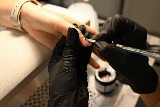 Manicurist in black gloves carefully applies brown nail polish on client’s nails during a manicure session at a beauty salon - Powered by Adobe