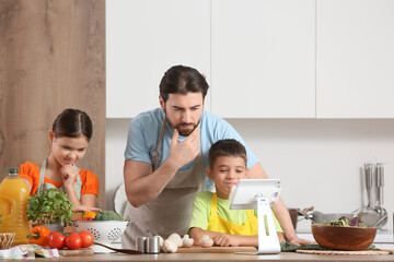Thoughtful father with his children and tablet computer cooking in kitchen