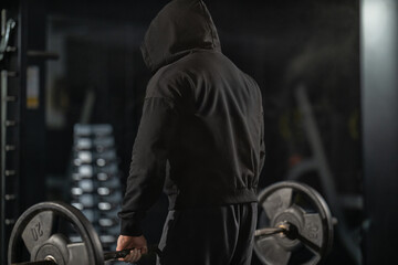 A man wearing a hooded sweatshirt prepares to lift heavy weights in a gym. The atmosphere is focused and intense as he concentrates on his deadlift technique during a workout session.