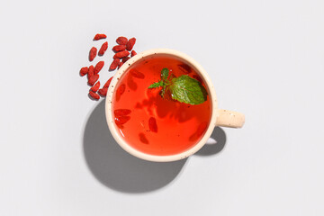 Cup of hot goji tea with mint and berries on grey background
