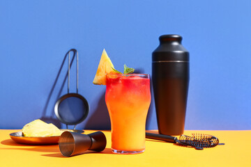 Glass of tasty Mai Tai cocktail garnished with pineapple and mint on orange table against blue...